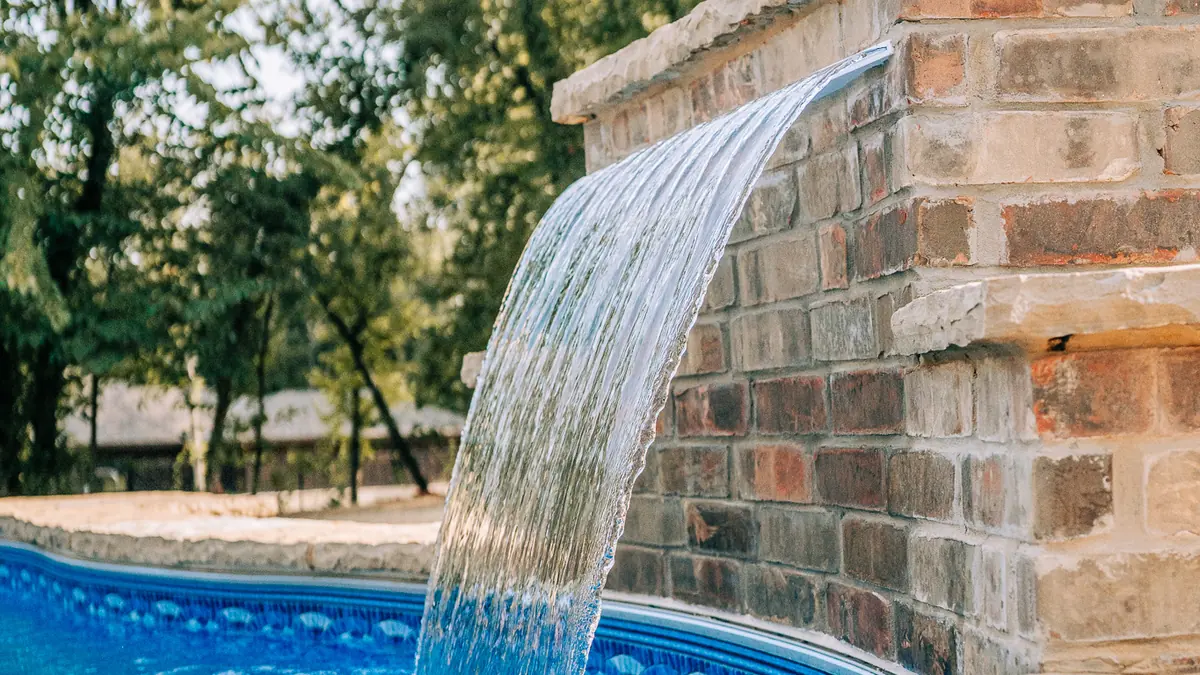 Brick water feature wall with sheer descent waterfall over a pool
